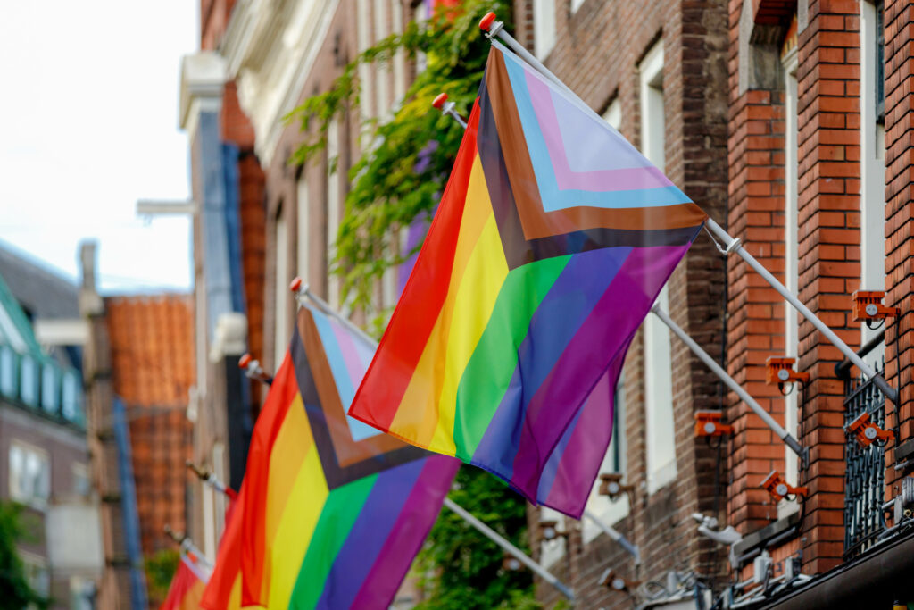 Progress pride flag (new design of rainbow flag) waving in the air with blue sky